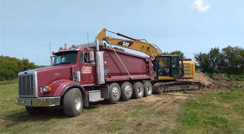 Red dump trucking being filled with dirty by an excavator
